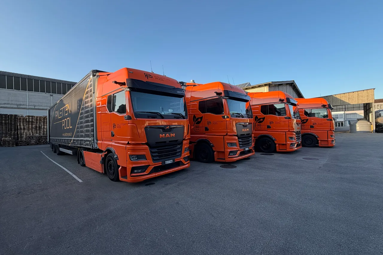 Vier orange Lastwagen der Paletten-Pool GmbH auf dem Werkhof in Oberbipp; die drei hinteren tragen das Elektro-Signet, der vordere mit dem Auflieger ist der Diesel-Lastwagen